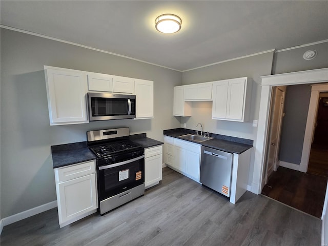 kitchen featuring a sink, wood finished floors, stainless steel appliances, and white cabinetry