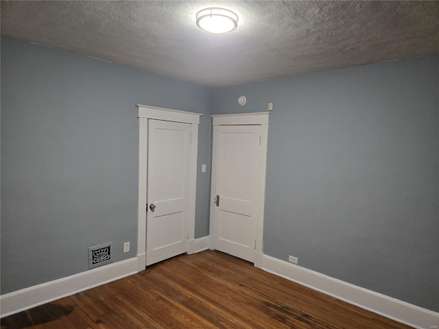 unfurnished room with dark wood finished floors, visible vents, a textured ceiling, and baseboards