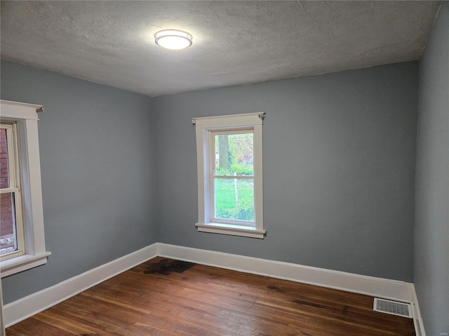 spare room featuring baseboards, visible vents, a textured ceiling, and dark wood-type flooring