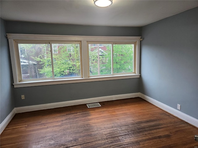 empty room featuring baseboards, visible vents, a healthy amount of sunlight, and dark wood-type flooring