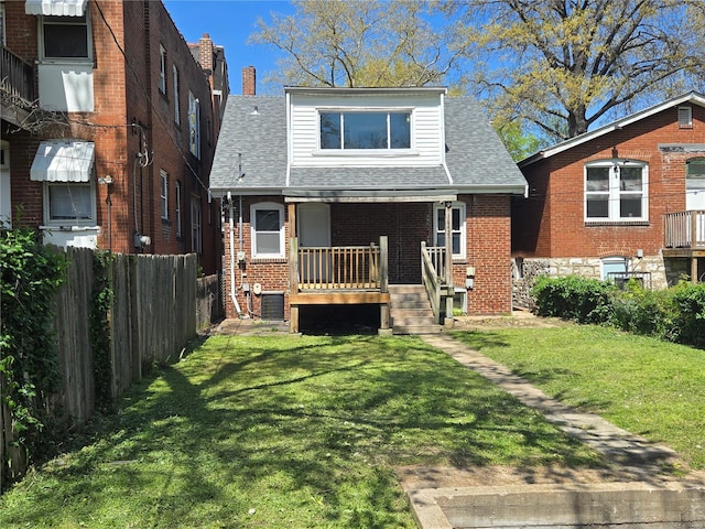 back of house featuring brick siding, fence, a porch, and a lawn