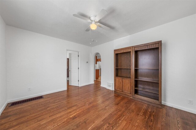 interior space with a ceiling fan, visible vents, arched walkways, wood finished floors, and baseboards