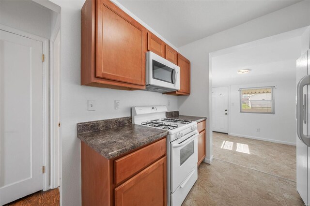 kitchen featuring dark countertops, brown cabinetry, and white appliances