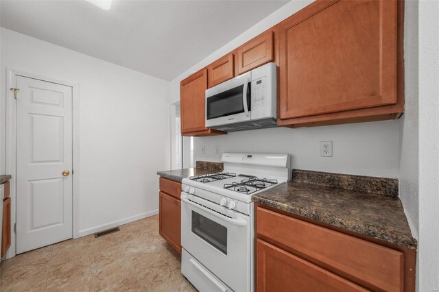 kitchen with brown cabinetry, visible vents, dark countertops, baseboards, and white appliances