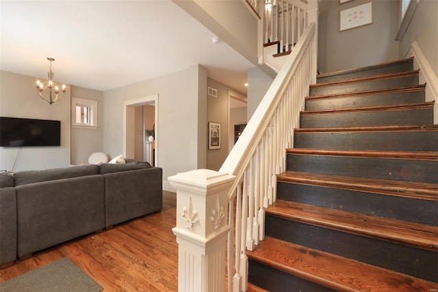stairs with an inviting chandelier, wood finished floors, and visible vents