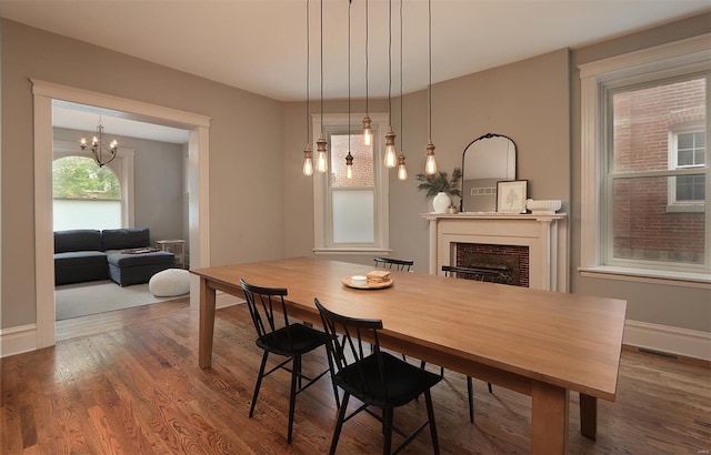 dining area featuring a notable chandelier, a fireplace, baseboards, wood finished floors, and visible vents