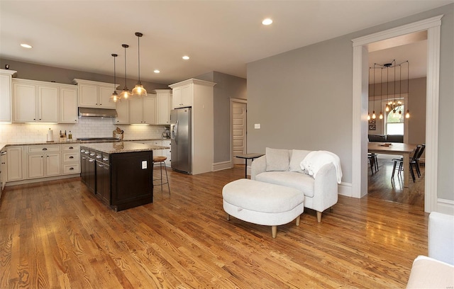 kitchen featuring a kitchen bar, appliances with stainless steel finishes, tasteful backsplash, light wood finished floors, and under cabinet range hood