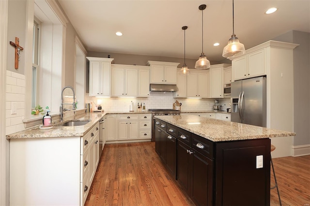 kitchen featuring wood finished floors, a breakfast bar area, under cabinet range hood, a sink, and appliances with stainless steel finishes