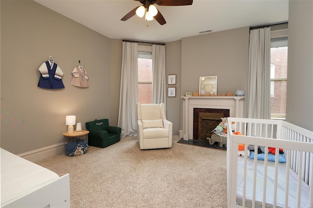 carpeted bedroom featuring visible vents, a fireplace with flush hearth, a nursery area, and multiple windows