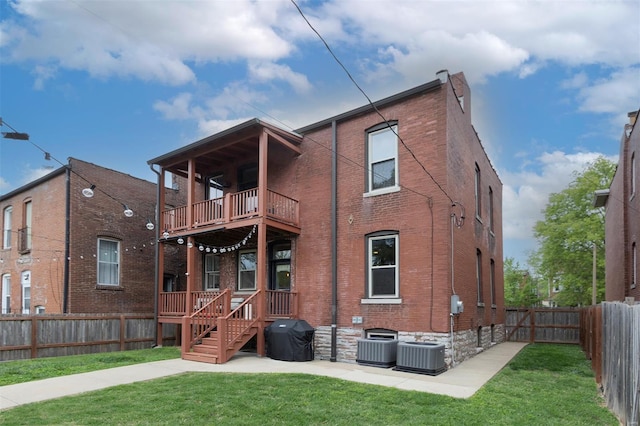 rear view of property with a fenced backyard, a yard, brick siding, and a balcony