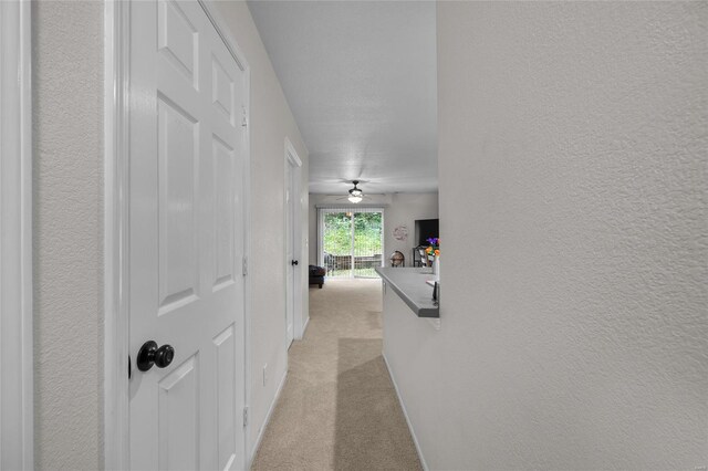 corridor with light colored carpet, a textured wall, and baseboards