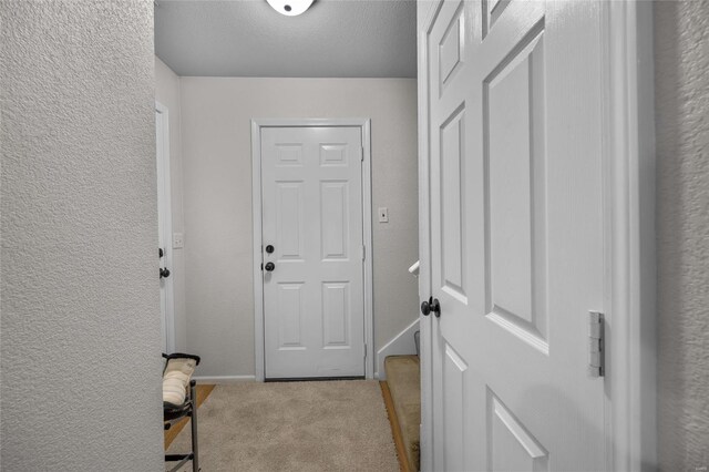 entryway featuring carpet floors, a textured ceiling, a textured wall, and baseboards