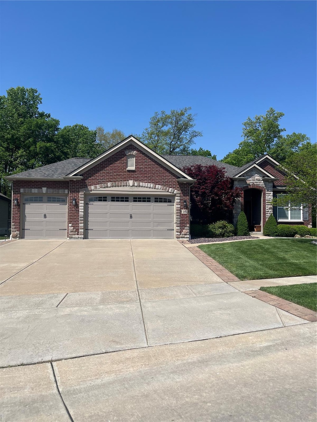 ranch-style house with concrete driveway, brick siding, an attached garage, and a front lawn