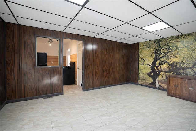 unfurnished room with visible vents, wood walls, an accent wall, and a drop ceiling