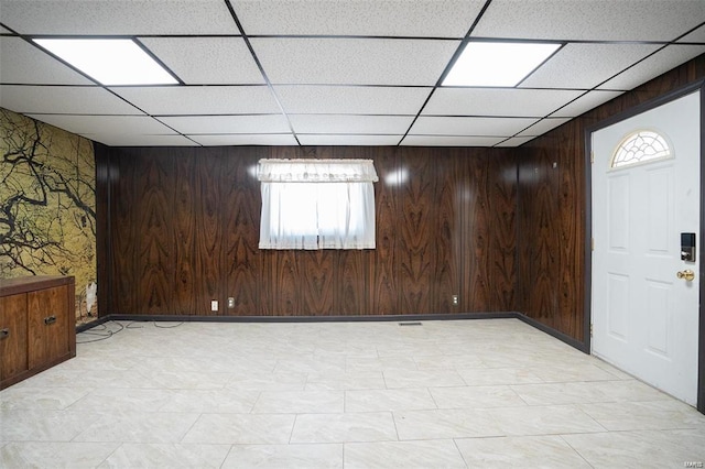 below grade area featuring light floors, a paneled ceiling, wooden walls, and wallpapered walls