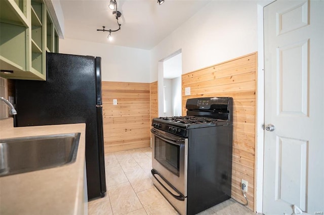 kitchen featuring a sink, stainless steel gas range oven, wood walls, freestanding refrigerator, and green cabinets