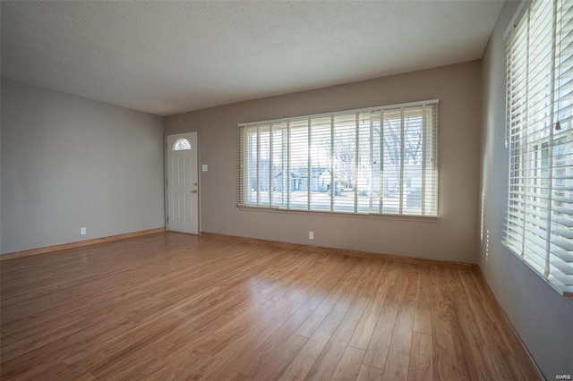 unfurnished living room featuring a textured ceiling, baseboards, and light wood finished floors