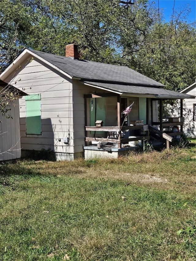 back of property featuring a lawn, covered porch, a chimney, and roof with shingles