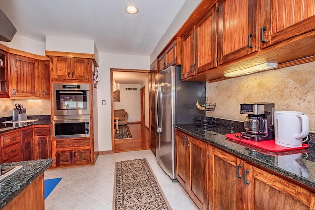 kitchen featuring brown cabinets, appliances with stainless steel finishes, decorative backsplash, and dark stone countertops