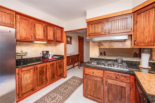 kitchen featuring under cabinet range hood, appliances with stainless steel finishes, brown cabinetry, and tasteful backsplash