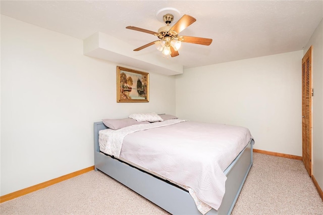 bedroom with a closet, baseboards, a ceiling fan, and light colored carpet