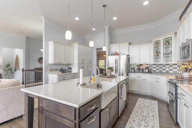 kitchen featuring appliances with stainless steel finishes, a sink, white cabinetry, crown molding, and a center island with sink