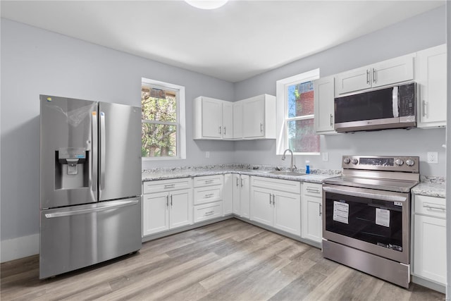 kitchen with appliances with stainless steel finishes, light wood-type flooring, white cabinets, and a sink