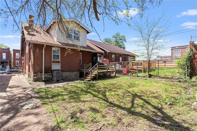 rear view of house with a wooden deck, brick siding, a lawn, a chimney, and fence