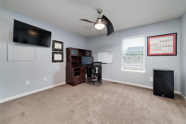 carpeted office space featuring baseboards and a ceiling fan