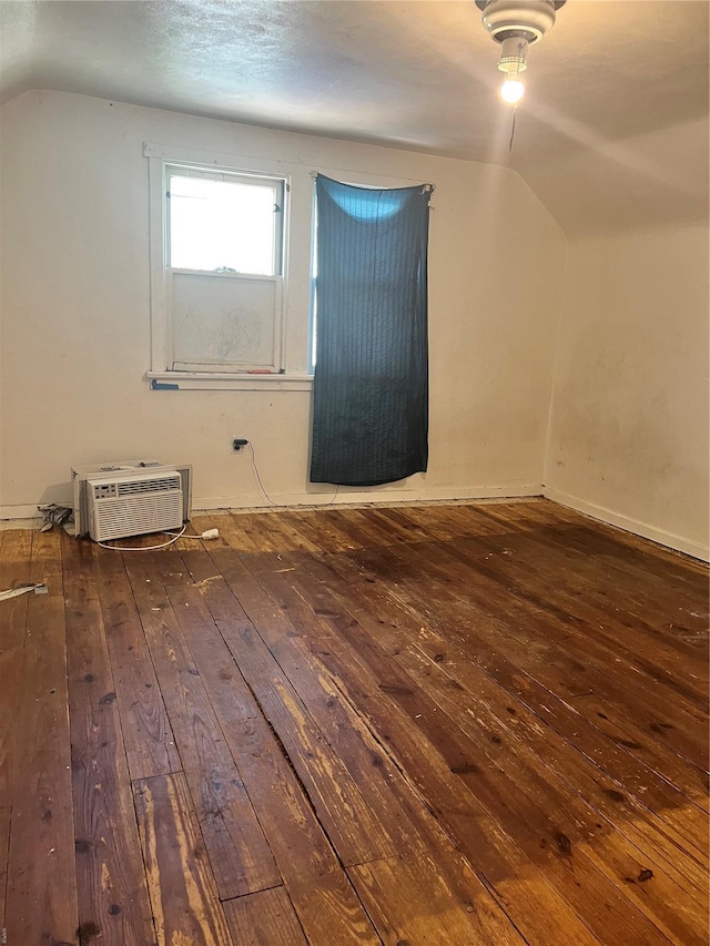 additional living space with a wall mounted AC, baseboards, wood-type flooring, and vaulted ceiling