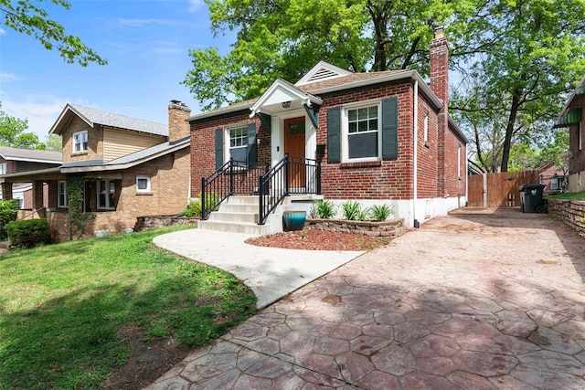 bungalow-style home featuring a chimney, concrete driveway, a front lawn, and brick siding
