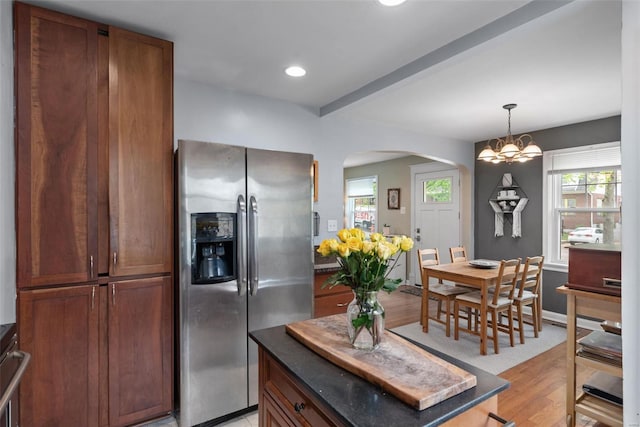 kitchen with stainless steel refrigerator with ice dispenser, arched walkways, dark countertops, and light wood-type flooring