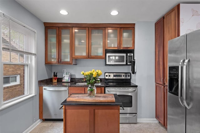 kitchen featuring glass insert cabinets, baseboards, a center island, brown cabinets, and stainless steel appliances
