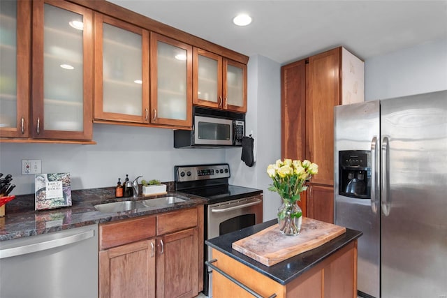 kitchen featuring a sink, dark stone counters, stainless steel appliances, and brown cabinets