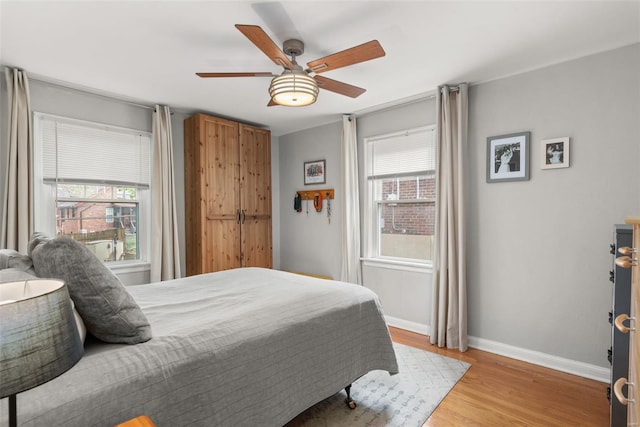 bedroom with baseboards, multiple windows, ceiling fan, and light wood-style floors