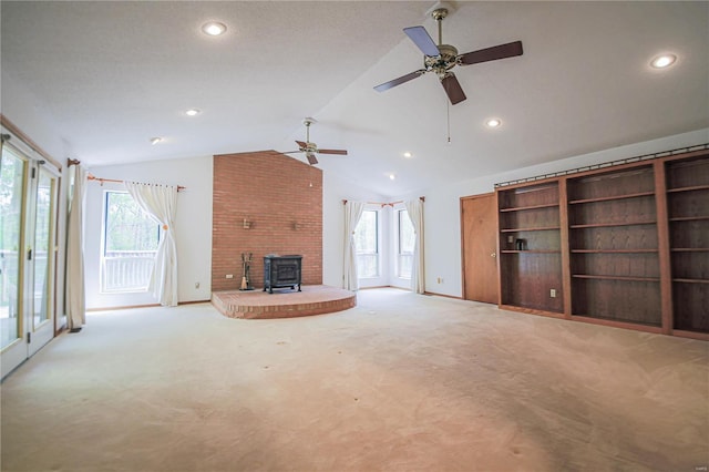 unfurnished living room featuring a wood stove, carpet flooring, a ceiling fan, vaulted ceiling, and plenty of natural light