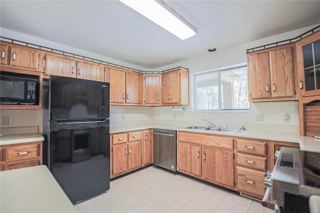 kitchen with brown cabinets, a sink, light countertops, black appliances, and backsplash