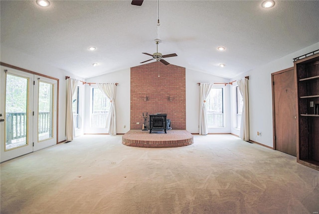 unfurnished living room featuring a wood stove, ceiling fan, vaulted ceiling, and light colored carpet