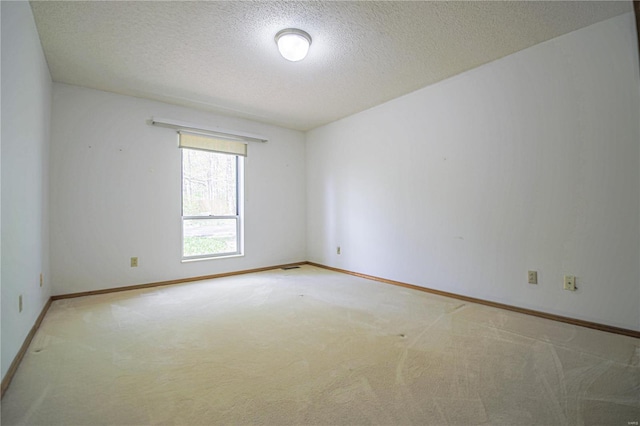 unfurnished room with light colored carpet, baseboards, and a textured ceiling