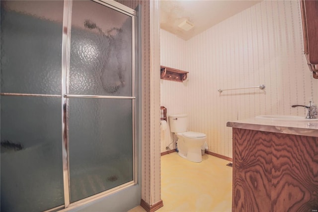 bathroom with wallpapered walls, a shower with door, toilet, vanity, and baseboards
