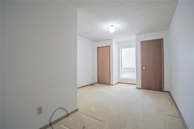 empty room with a textured ceiling, light carpet, and baseboards