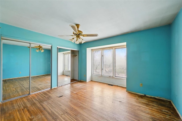 unfurnished bedroom with baseboards, multiple closets, ceiling fan, and hardwood / wood-style floors