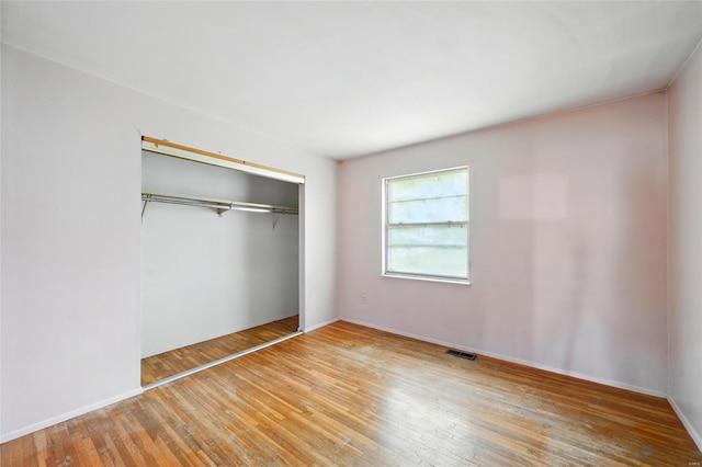 unfurnished bedroom with wood-type flooring, baseboards, visible vents, and a closet
