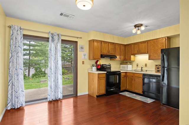 kitchen with a sink, visible vents, light countertops, under cabinet range hood, and black appliances