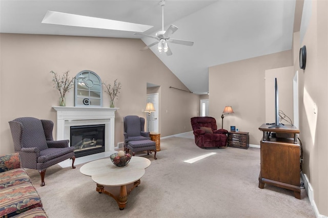carpeted living room with a glass covered fireplace, ceiling fan, baseboards, and vaulted ceiling with skylight