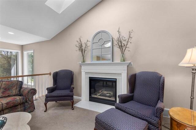 carpeted living area with baseboards, vaulted ceiling with skylight, a fireplace with flush hearth, and recessed lighting