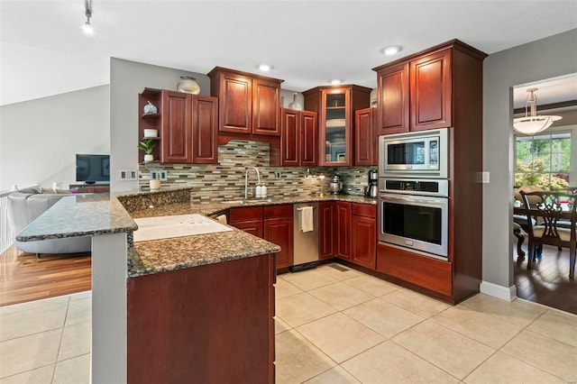kitchen featuring backsplash, appliances with stainless steel finishes, a sink, light tile patterned floors, and a peninsula