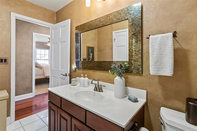 bathroom featuring tile patterned flooring, vanity, a textured wall, toilet, and ensuite bath