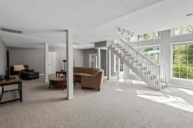 carpeted living area featuring a textured ceiling, visible vents, rail lighting, baseboards, and stairs