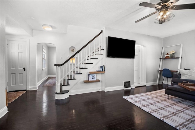 living area featuring arched walkways, ceiling fan, stairs, and wood finished floors